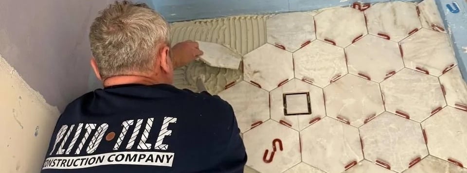 Plito Tile installer setting hexagonal marble-look floor tile with a leveling system
