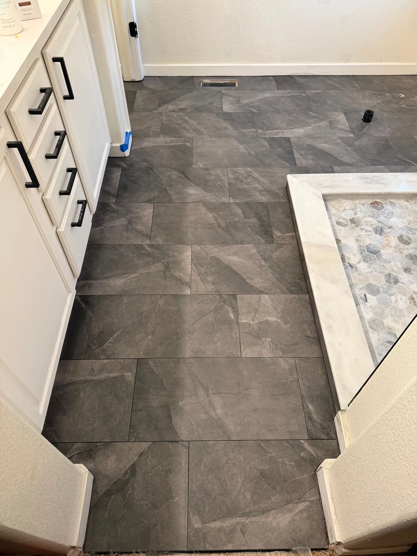 Dark charcoal large-format bathroom floor with a white marble shower curb and hex mosaic shower floor