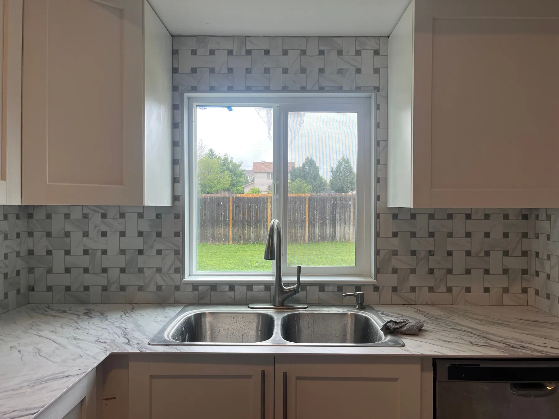 Marble basketweave kitchen backsplash wrapping a window above a double sink