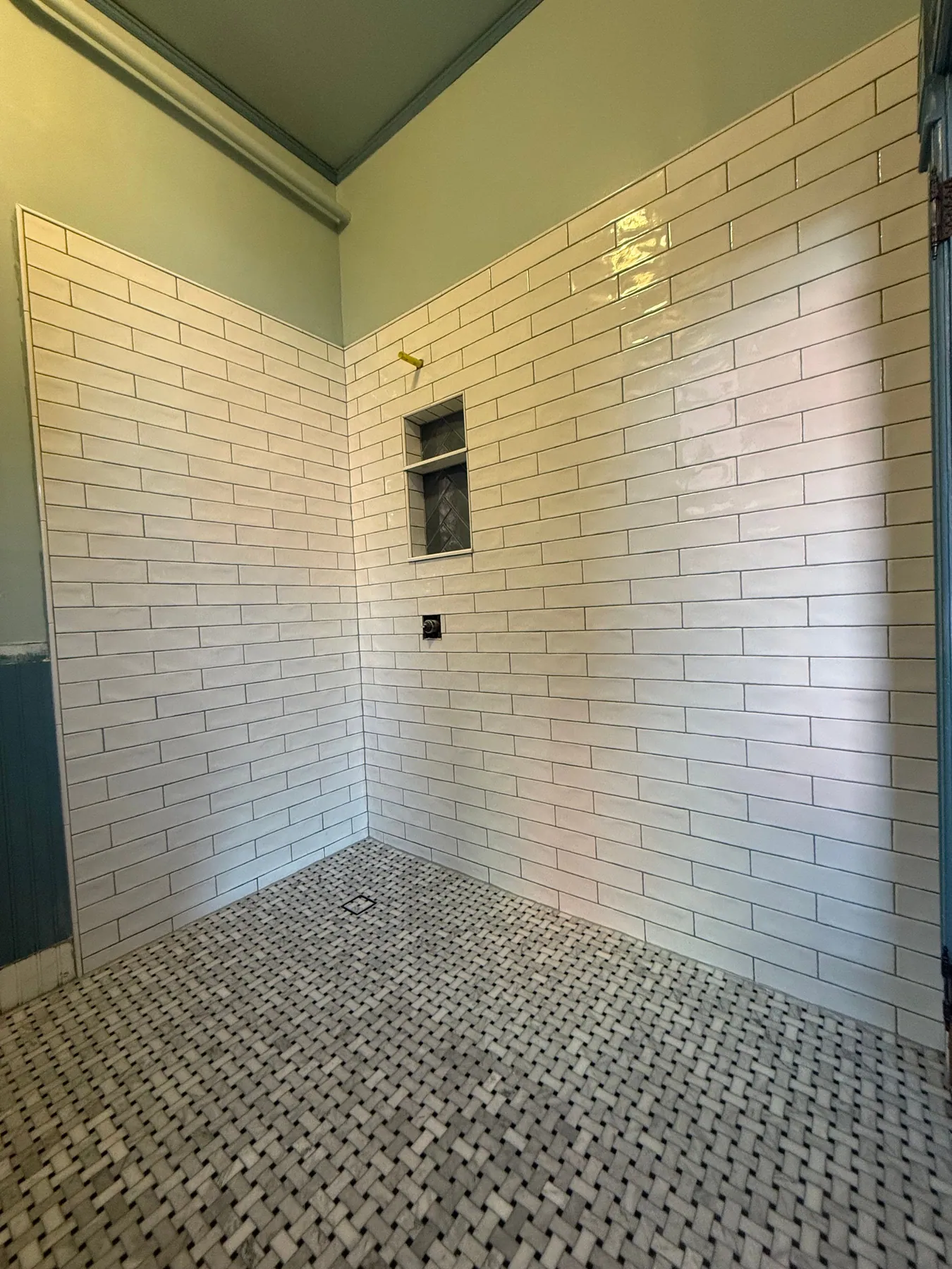 Walk-in shower with white subway wall tile, basketweave mosaic floor, and a recessed niche