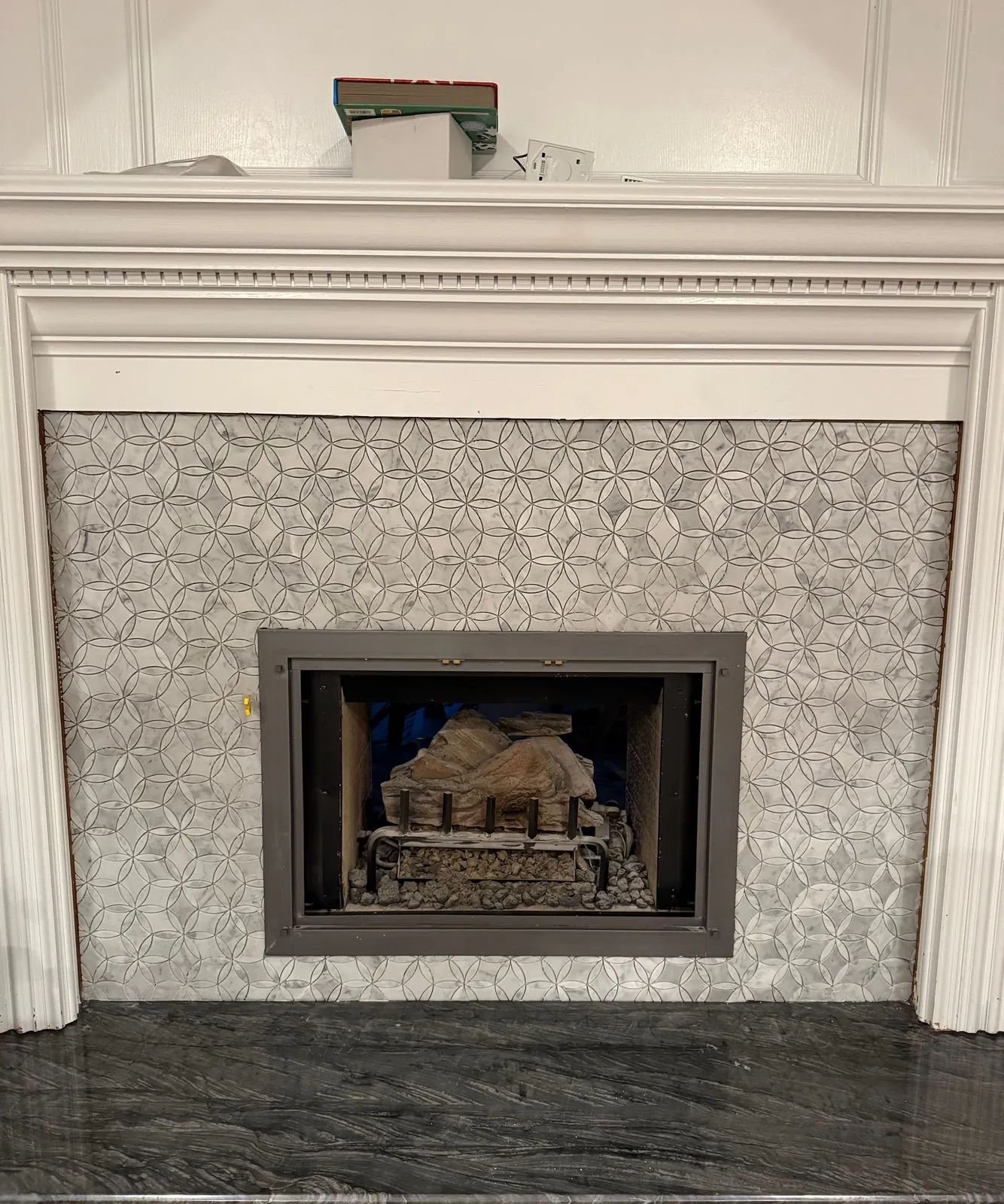 Fireplace surround in geometric marble mosaic tile with a dark stone hearth