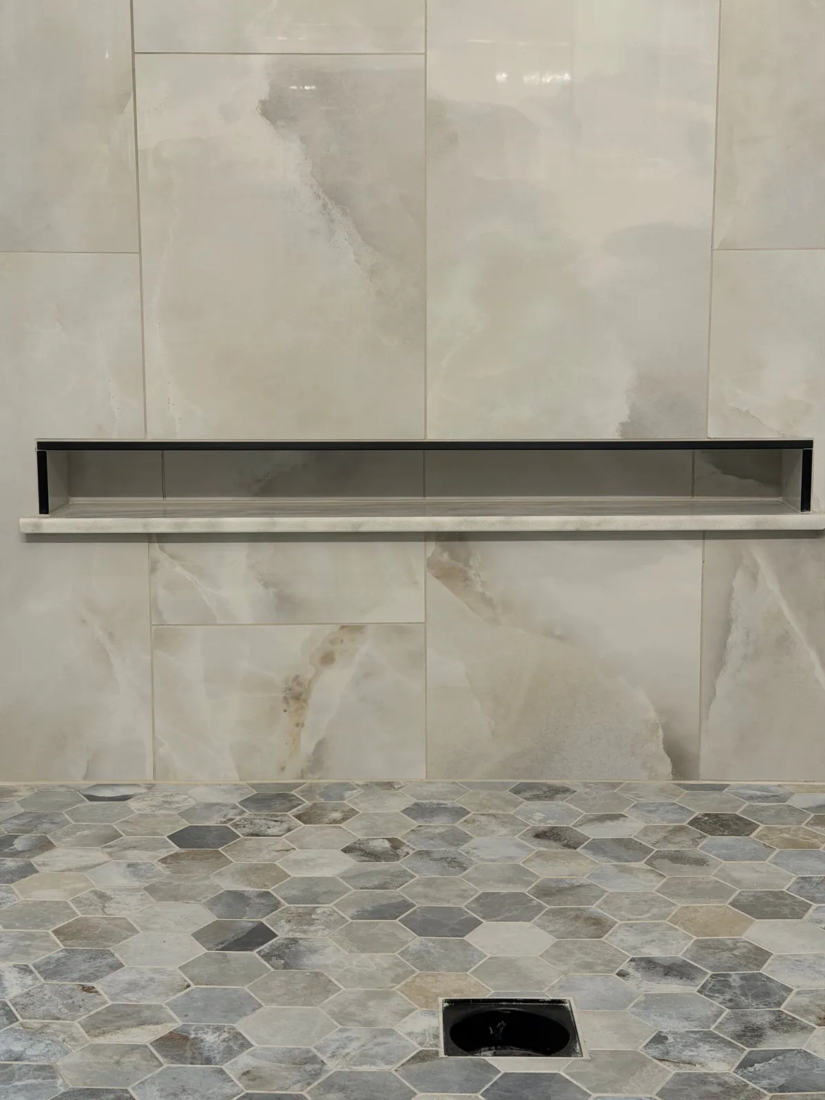 Shower wall with a recessed niche in marble-look tile above a hex mosaic floor