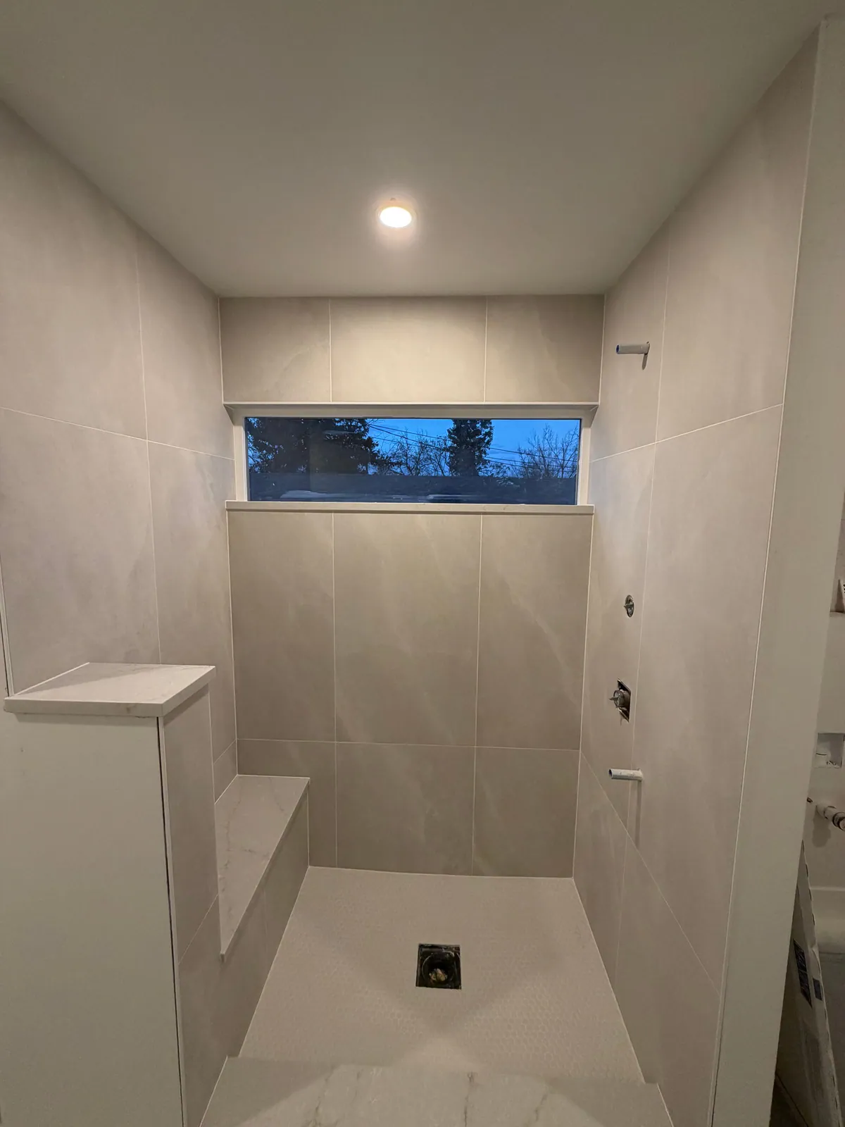 Walk-in shower with large-format wall tile, hex mosaic floor, and a built-in tiled bench
